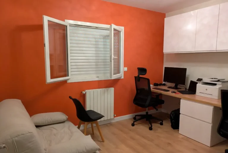 photo de la chambre aménagée en bureau pour 2 personnes. mur de la fenêtre en orange, meubles de rangement blanc